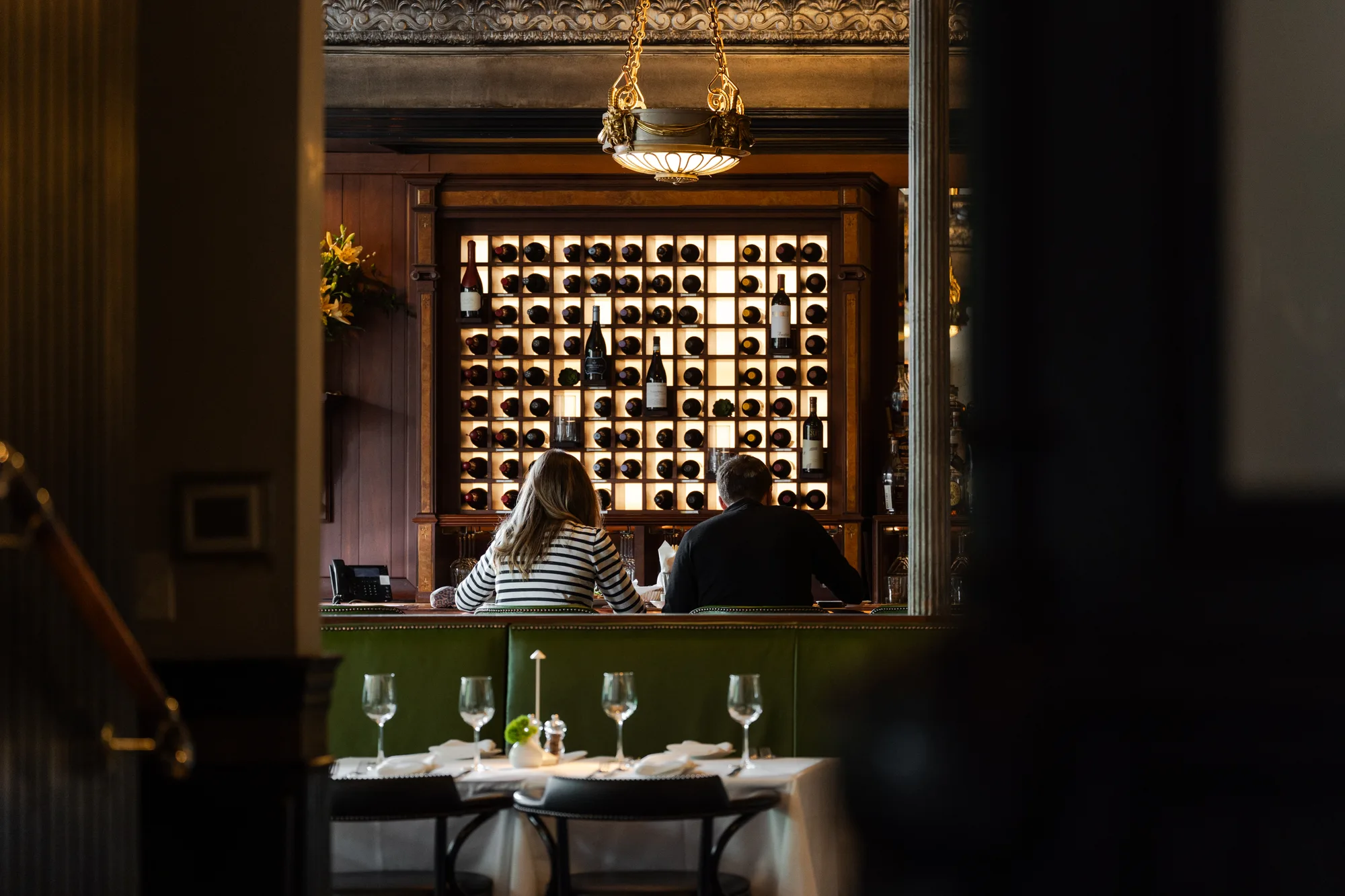 Guests at the bar under a lit wine wall
