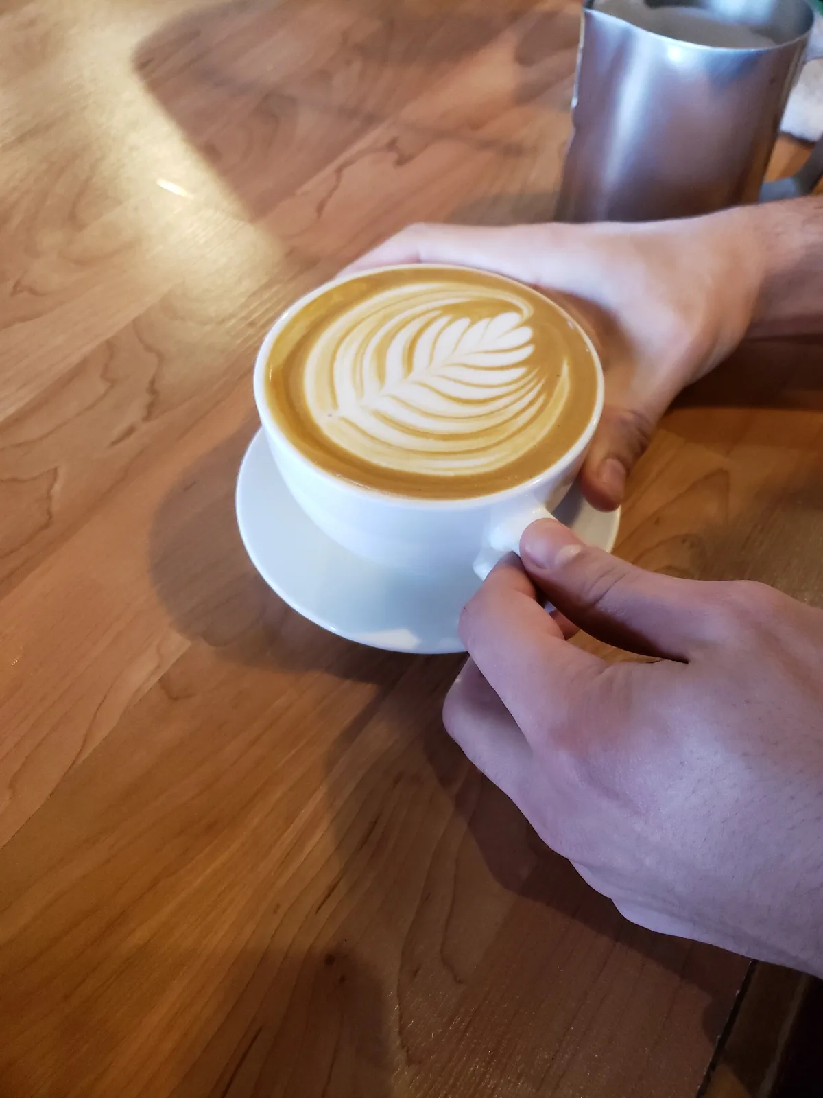 Latte art in a ceramic cup held above a wooden floor