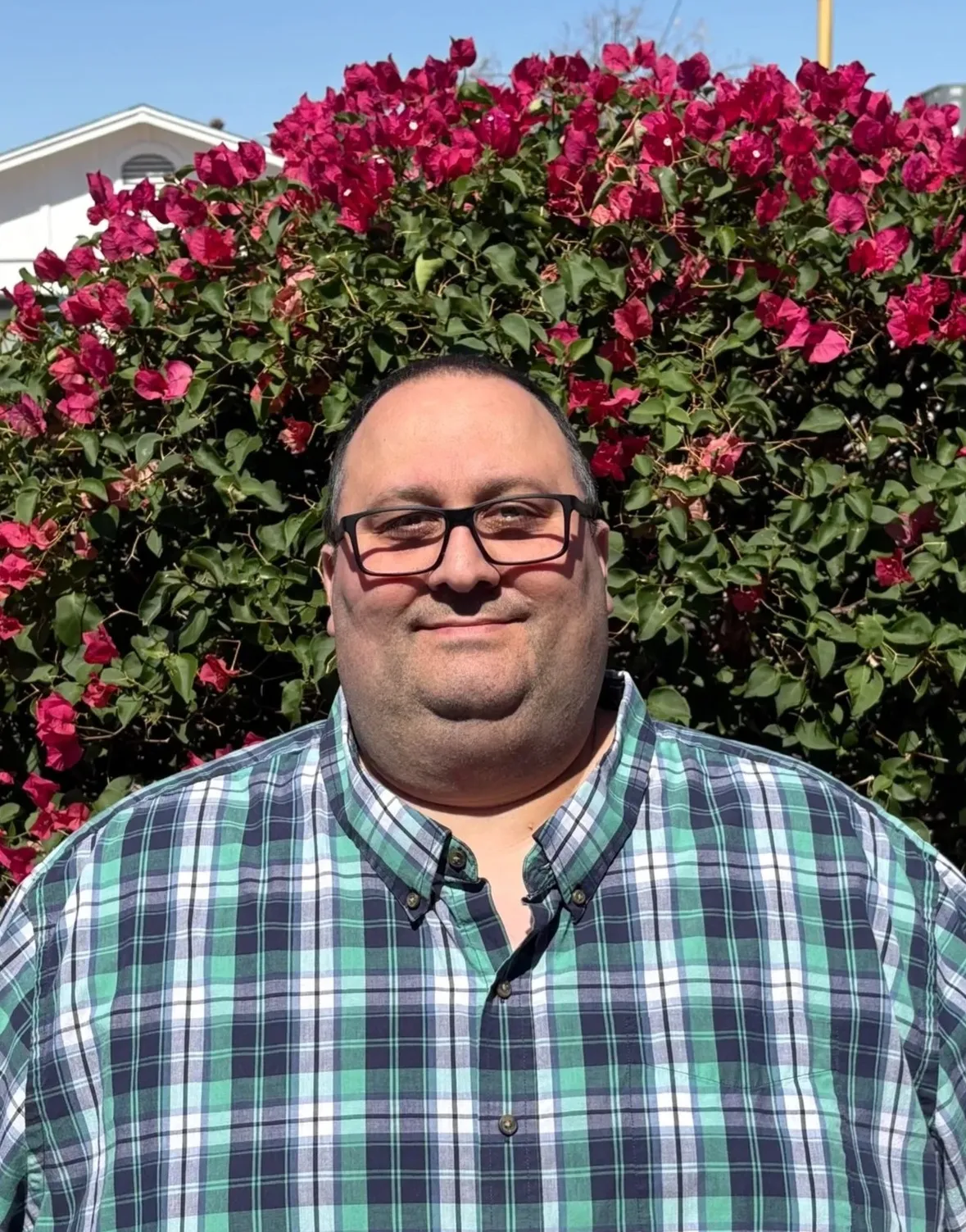 Rob Robinson in a plaid shirt in front of blooming bougainvillea