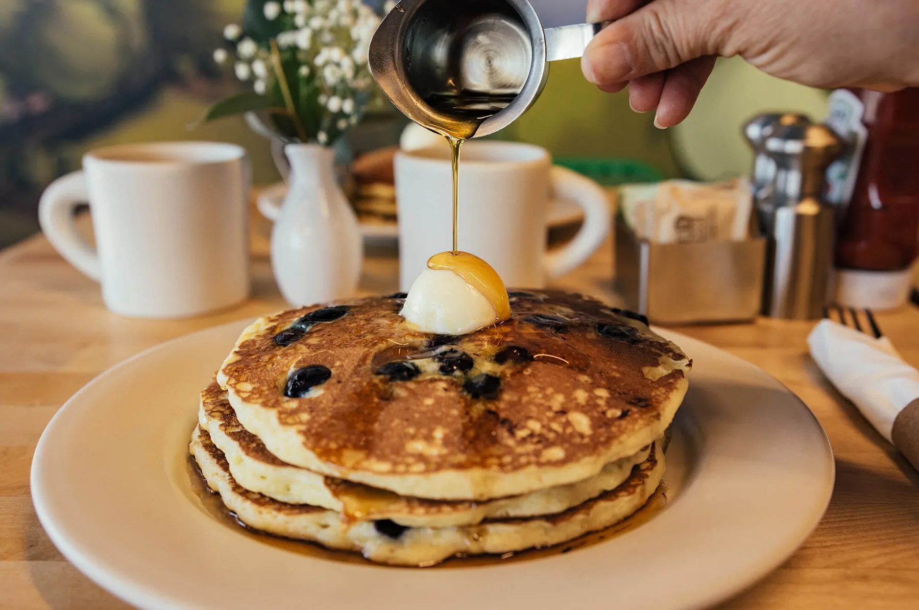 Syrup pouring over a stack of blueberry griddlecakes
