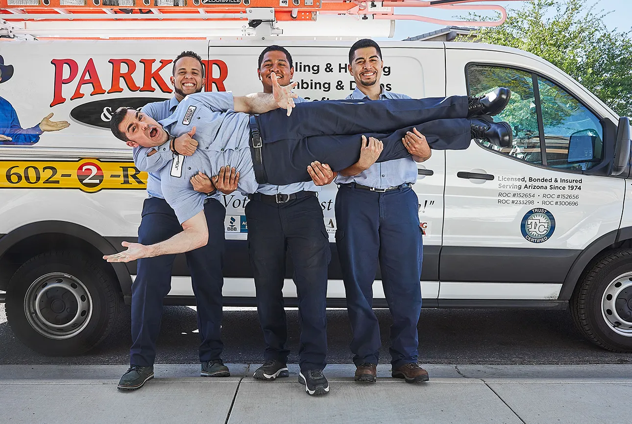 Four Parker & Sons technicians clowning around in front of a company van