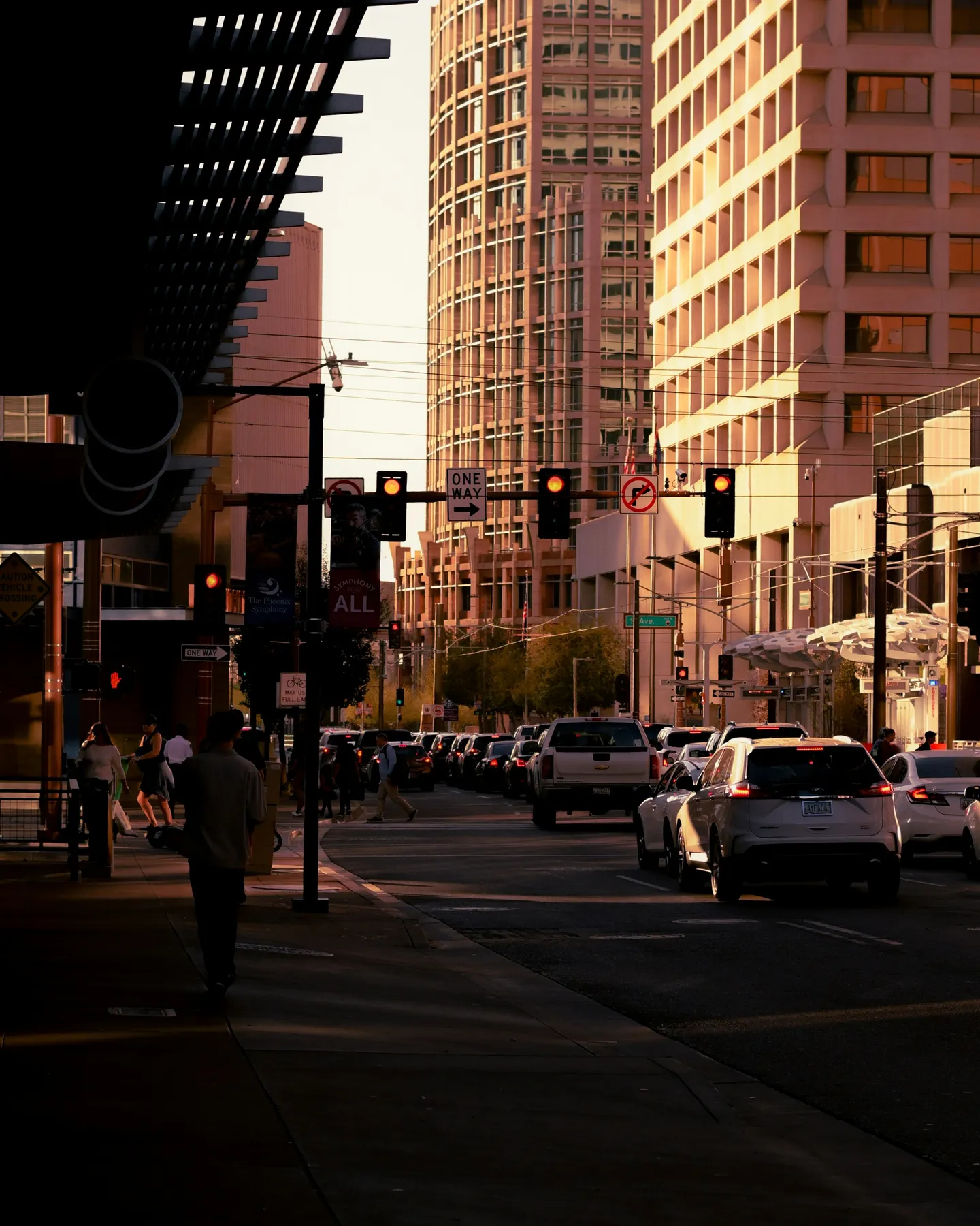 People crossing a downtown Phoenix street at golden hour, between office towers