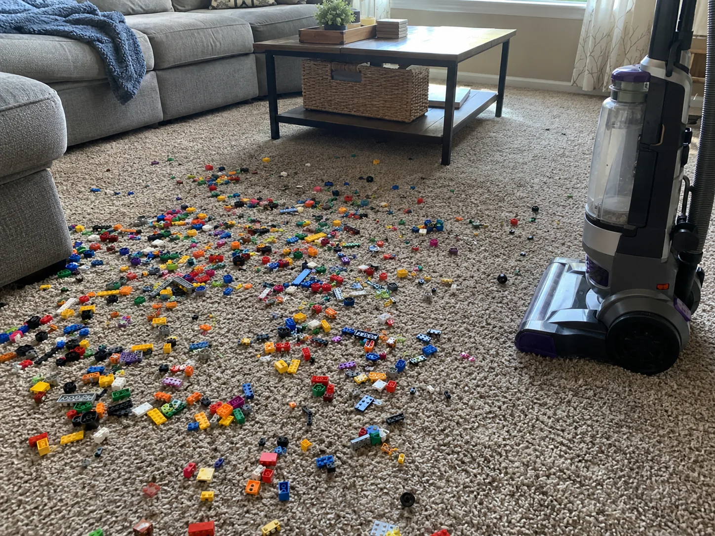 Hundreds of tiny toy building pieces scattered on a carpet next to a vacuum