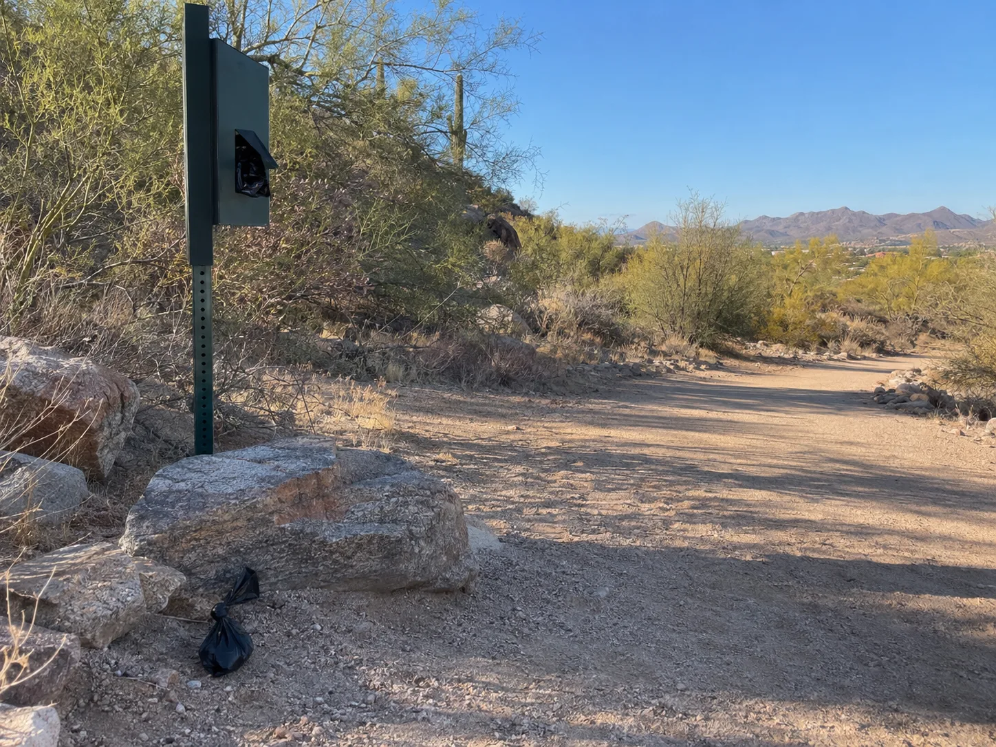 A desert walking trail with a dog waste bag station and a bag left on the ground
